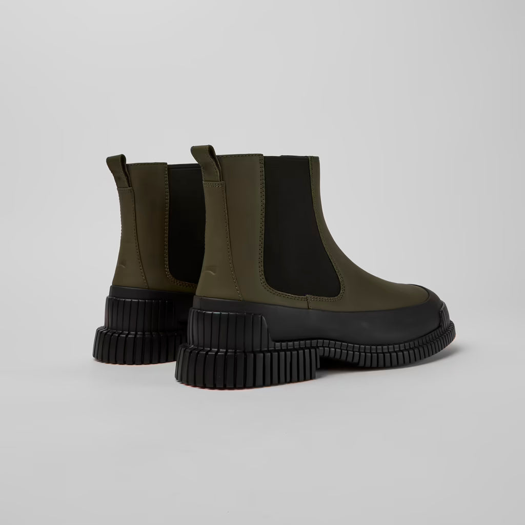 Pair of green Chelsea boots with black soles on a light gray background