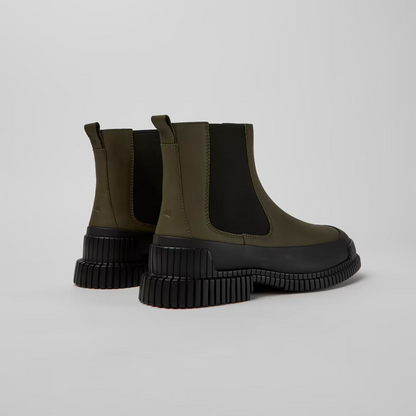 Pair of green Chelsea boots with black soles on a light gray background