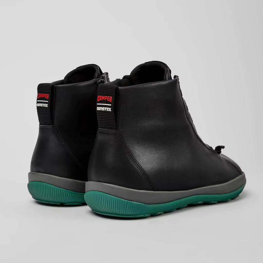 Black ankle boots with green soles on a light gray background