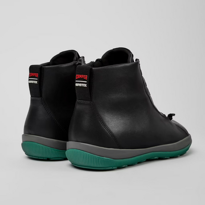 Black ankle boots with green soles on a light gray background